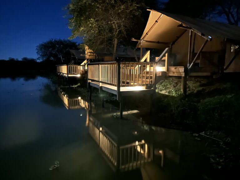 Glamping tents on raised wooden decks reflected in the Rio Grande at night