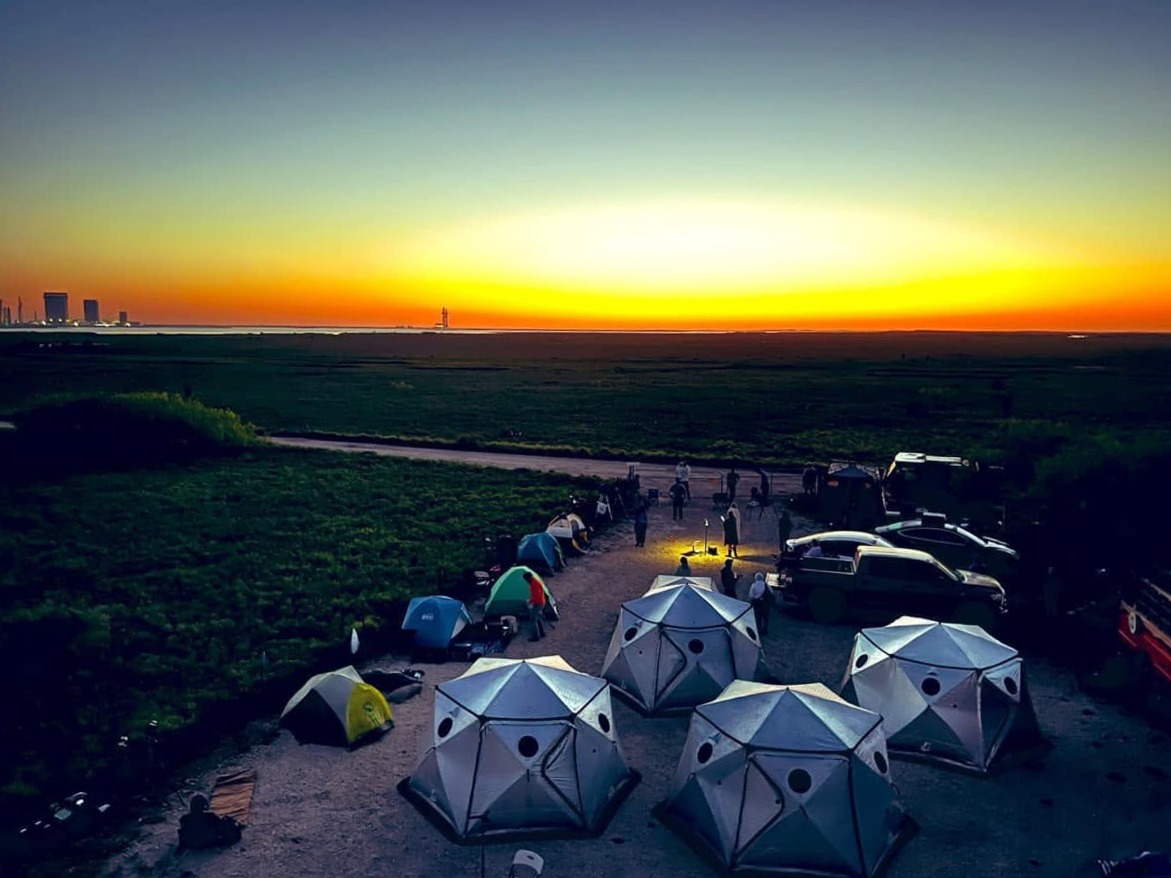 Rocket Ranch tents at sunset with Starbase on the horizon